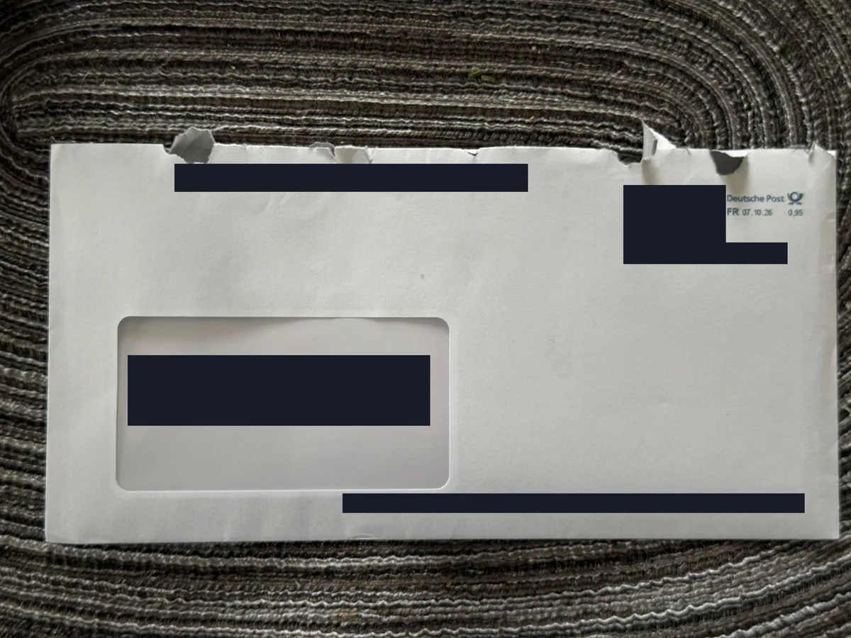 Weißer Fensterumschlag mit Freistempel der Deutschen Post vom 07.10.26, Anschrift im Fenster und alle Codes mit dunklen Balken unkenntlich gemacht